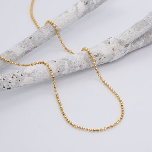 Kette aus kleinen, goldenen Kugeln, mit einem weißen Ast dekoriert.