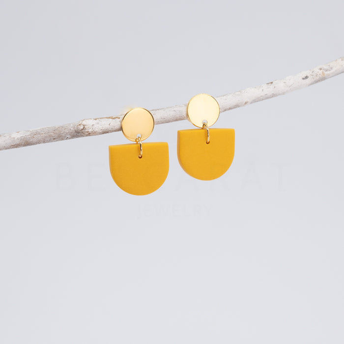 Ohrringe an Zweig aufgehängt. Goldenes Oberteil mit Anhänger in Gelb.