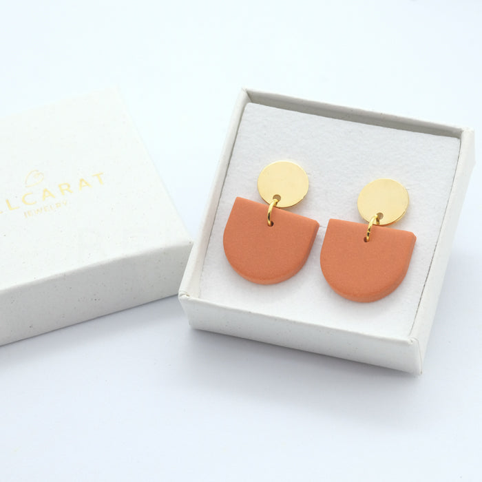 Ohrringe in Orange mit goldenem Oberteil, in einer Schachtel liegend.